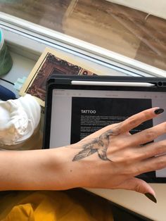 a woman's hand with tattoos on her left arm is holding an open laptop computer