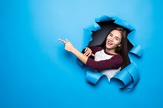 a woman pointing at something through a hole in the blue wall with torn paper on it