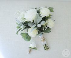 a bridal bouquet with white flowers and greenery hanging from the side of a wall