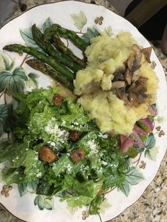 a plate with asparagus, mashed potatoes and green salad on it sitting on a table