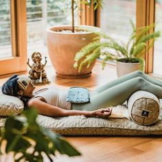 a woman laying on top of a pillow in front of a potted plant next to a window