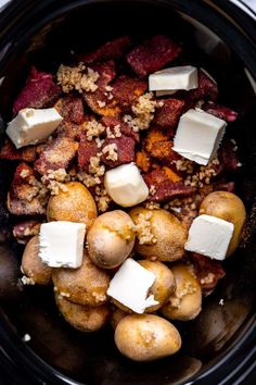 crock pot filled with potatoes, meat and cheese on top of some breadcrumbs