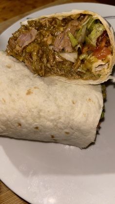 two burritos on a white plate sitting on a wooden table