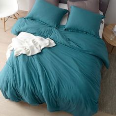 an unmade bed with teal colored sheets and pillows on the floor next to a night stand