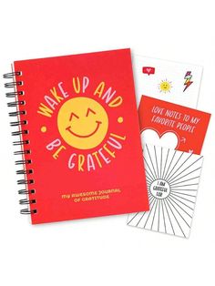 a red notebook with the words wake up and be grateful written on it next to an orange spiral notebook