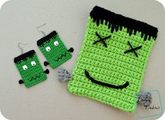 a crocheted bag with two green faces on it next to some earring and earrings