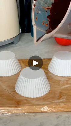 two white plastic cups sitting on top of a wooden board next to a blender