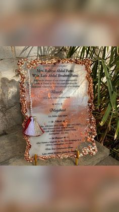 a plaque with a tassel on it sitting in front of some rocks and plants