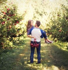 a man carrying a woman in his arms through an apple tree filled with red apples