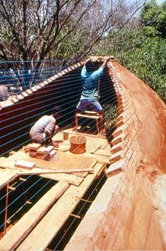 two men working on the side of a building with wood and wire fencing around it