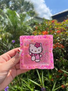 a hand holding up a pink hello kitty glass block with sprinkles on it