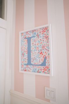 the letter j is hanging on the wall next to a light switch and striped wallpaper