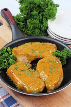 two pieces of meat in a pan with sauce and parsley on the side next to plates