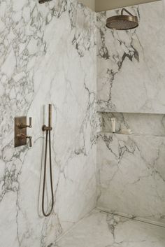 a bathroom with marble walls and flooring, shower head and hand held faucet