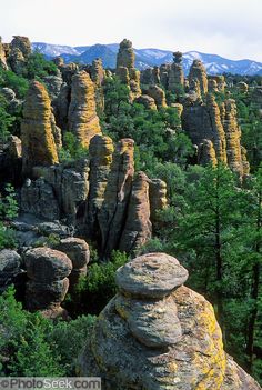 the rocky landscape is surrounded by green trees and tall rock formations with snow capped mountains in the distance