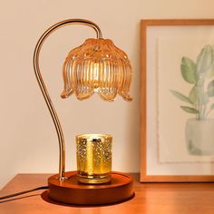 a glass lamp on a wooden table next to a framed photograph and a gold candle holder