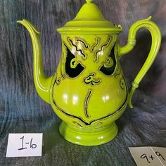 a green teapot with a face painted on it next to two numbered cards and numbers