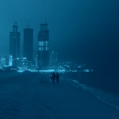 two people are walking on the beach in the dark with buildings in the background at night