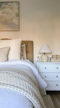 a white bed sitting next to a dresser and lamp