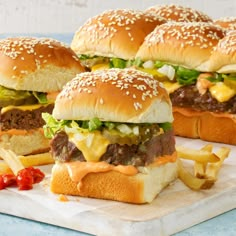 three hamburgers with cheese, lettuce and tomato on a wooden cutting board