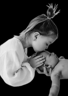 a black and white photo of a woman kissing a baby's head with her hands