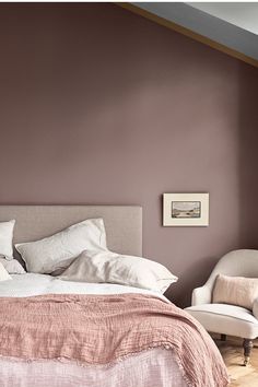 a bed sitting in a bedroom next to a white chair and pink walls with text overlay