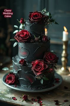 a three tiered black wedding cake with red roses on the side and candles in the background