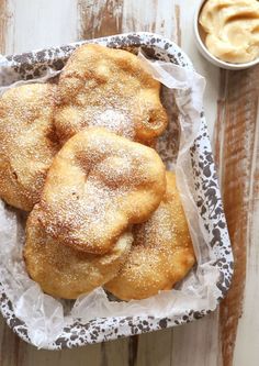 powdered sugar covered pastries in a basket next to a bowl of dipping sauce