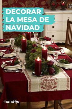 the table is set for christmas dinner with candles on it and red napkins, surrounded by greenery