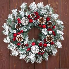 a christmas wreath with pine cones and red berries hanging on a wooden wall next to a fence