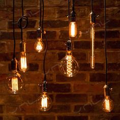 several light bulbs hanging from the ceiling in front of a brick wall with wires attached to them