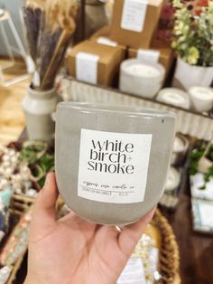 a person holding up a white candle in front of some flowers and other things on the table