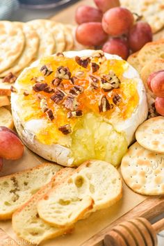 cheese and crackers on a wooden platter with grapes, nuts, and bread