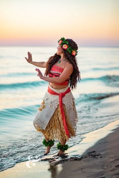 a woman in a hula skirt standing on the beach with her arms out to the side