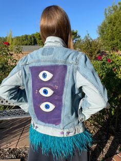 the back of a woman wearing a jean jacket with eye patches and fringes on it