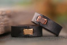 two black leather rings with gold accents on them sitting on a wooden table next to a rock