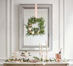 a christmas wreath is hanging on the wall above a buffet table with candles and desserts