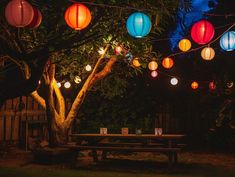 colorful paper lanterns hanging over a picnic table under a tree in the dark night time