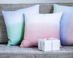 a couch with three pillows and a gift box on the pillow case next to it