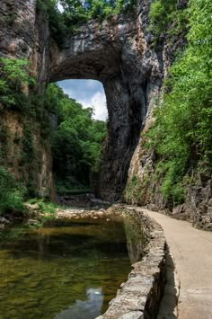 an arch in the side of a mountain with water running underneath it and people walking on either side