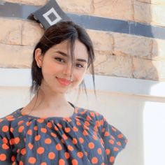 a young woman standing in front of a brick wall with an orange polka dot top