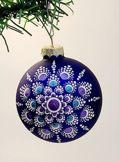 a blue ornament hanging from a tree branch with white and purple designs on it