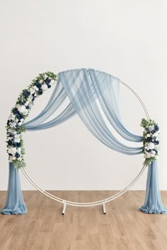 a white and blue wedding arch with flowers on the top, draped in light blue fabric