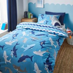 a blue bed with shark print on it in a child's bedroom, next to a window