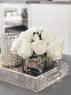 white roses are in a silver vase on a table with other decorations and lights around it