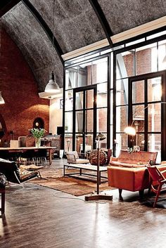 a living room filled with lots of furniture next to tall glass windows on top of a wooden floor