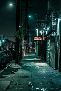 an empty city street at night with cars parked on the side walk and closed doors