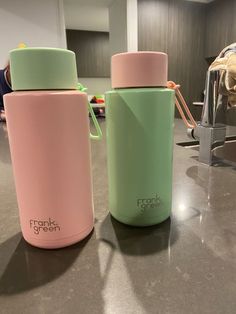 two pink and green insulated water bottles sitting on a counter