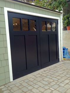 a black garage door with two windows on the outside and brick walkway next to it