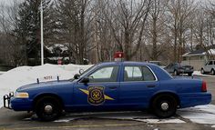 a police car is parked in the parking lot with snow on the ground and trees behind it